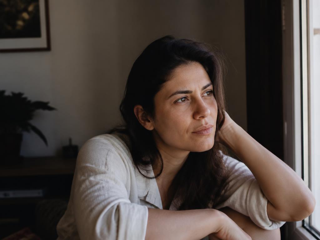 Mulher pensativa junto à janela lidando com alterações hormonais